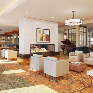 A modern hotel lobby with comfortable seating, a grand piano, and a fireplace.