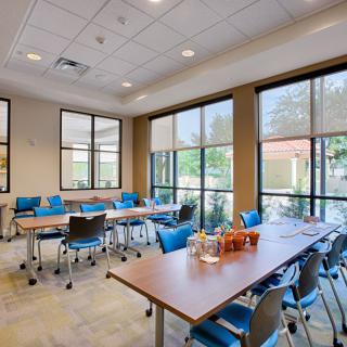 A bright conference room with tables and chairs arranged for a meeting, illuminated by natural light from large windows.