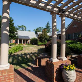 A serene outdoor area with a pergola and columns, surrounded by lush gardens and brick pathways.