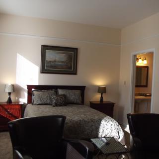 A cozy bedroom with elegant decor, featuring a bed, side tables, lamps, and a framed painting on the wall.