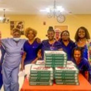 A group of healthcare professionals in uniform gathered around a table with stacks of pizza boxes.