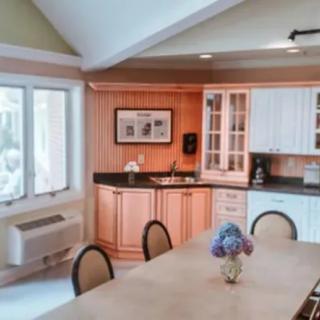 A cozy kitchen and dining area featuring a table with chairs, surrounded by cabinets and natural light from large windows.