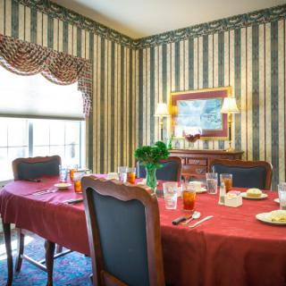 A cozy dining room with a red tablecloth, set for a meal, featuring striped wallpaper and elegant curtains.