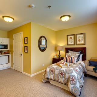 A cozy bedroom with a single bed, kitchenette, and warm yellow walls.