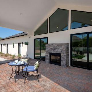 A modern covered patio with a stone fireplace, outdoor seating, and large windows.