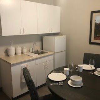 A small kitchen with a dining area, featuring white cabinets, a refrigerator, and a neatly set table.