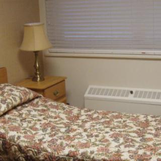 A simple bedroom with a single bed, nightstand, lamp, and window with closed blinds.