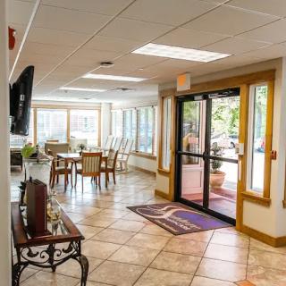 A welcoming lobby area with tiled flooring, tables and chairs, large windows letting in natural light, and a main entrance door.