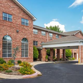 A brick exterior building with a landscaped entrance and covered driveway, possibly a hotel.