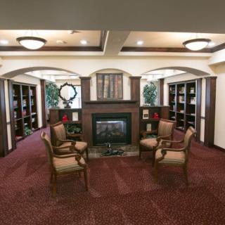 A cozy library with a central fireplace, surrounded by bookshelves and elegant seating.