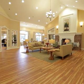 A spacious and elegant living room with wooden flooring, featuring comfortable sofas, a large coffee table, and a prominent fireplace under a stylish chandelier.