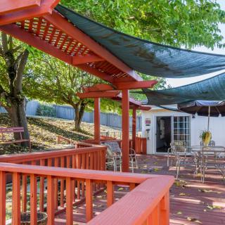 A cozy outdoor patio area with a pergola and seating, shaded by trees.