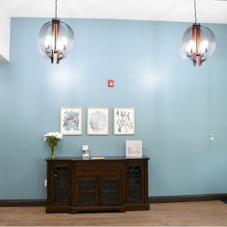 A stylish interior featuring a wooden cabinet, decorative wall art, and contemporary lighting against a soothing blue backdrop.