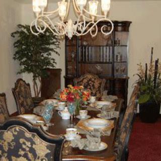 An elegantly set dining room table with a chandelier overhead and floral arrangements as centerpiece.