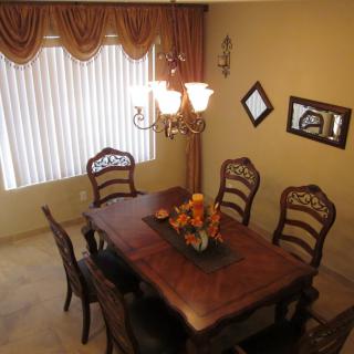 A well-decorated dining room featuring a wooden table with six chairs, a chandelier overhead, and elegant curtains.