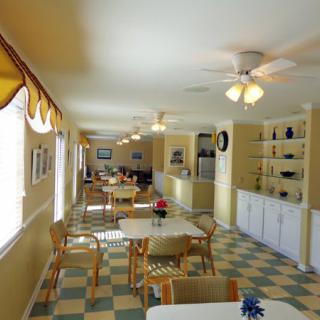 A bright dining room with checkered flooring and multiple tables and chairs arranged neatly.