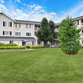 A residential apartment building with a well-maintained lawn and surrounding trees under a blue sky.