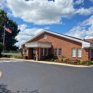 A brick building with an American flag flying outside, set against a backdrop of fluffy clouds and blue sky.