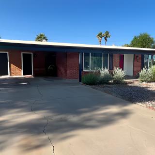 A mid-century single-story house with a driveway and landscaping under a clear blue sky.