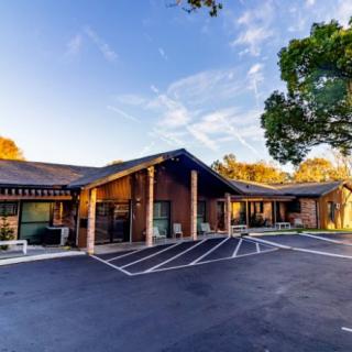 A modern building with a parking lot surrounded by trees under a clear sky.