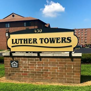 A sign for Luther Towers in front of a residential building.
