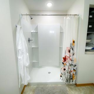 A modern bathroom featuring a walk-in shower with floral and white shower curtains, and a white robe hanging on the side.
