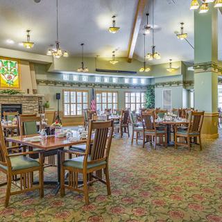 A spacious dining area with wooden tables and chairs, featuring elegant lighting and a cozy atmosphere.