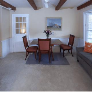 A cozy dining room with a table and chairs, featuring exposed beams and a painting on the wall.