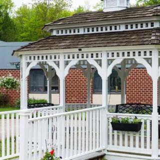 A white wooden gazebo in a garden setting with a brick wall background.