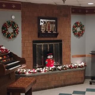 A cozy holiday-themed interior featuring a decorated fireplace, wreaths, and a cheerful snowman.