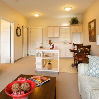 A cozy living room with a view of the kitchen, featuring modern furniture and warm lighting.