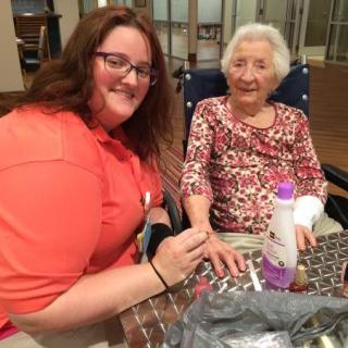 A caregiver is giving a manicure to an older adult, both smiling and enjoying their interaction.