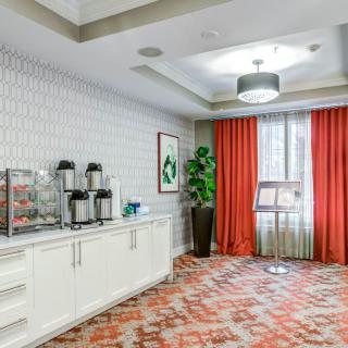 A stylish hotel lobby features a beverage station with coffee dispensers and an elegant carpeted floor.