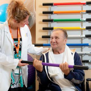 A healthcare professional assists an elderly man during a physical therapy session.