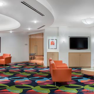 A modern lobby with colorful carpet and comfortable orange seating, featuring a television and artwork on the walls.