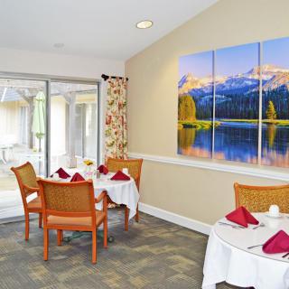 A cozy dining area with neatly set tables and vibrant landscape artwork on the wall.