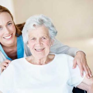 A caregiver smiles while supporting an elderly woman.
