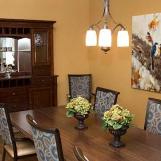 A well-furnished dining room featuring a wooden table with floral centerpieces, upholstered chairs, a decorative chandelier, and a cabinet with glassware.