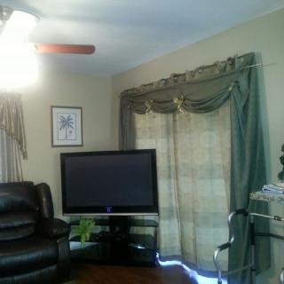 A cozy living room featuring a television, leather chair, and elegant curtains.