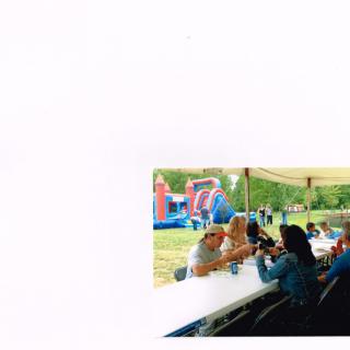 A group of people gathering under a tent at an outdoor event with a bouncy castle in the background.