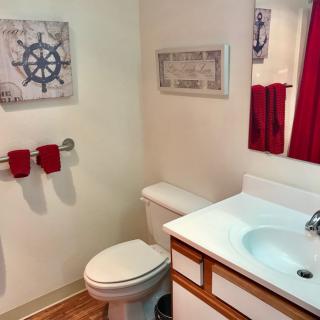 A small bathroom with nautical-themed decor, featuring a sink, toilet, mirror, and red towels.