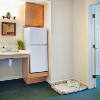 A small kitchenette with a refrigerator, sink, and a pet bed nearby.