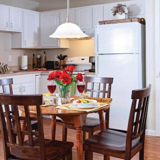 A cozy kitchen dining area with a wooden table, chairs, and a vase of flowers.