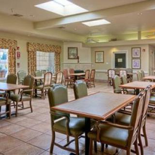 An empty dining room with multiple tables and chairs, featuring windows with curtains and overhead lighting.