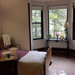 A cozy bedroom with a bed, windows, and a small table with a lamp.