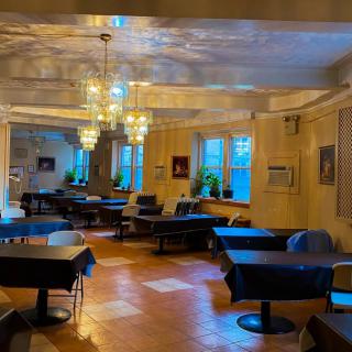 A cozy restaurant interior featuring elegantly set tables, chandeliers, and large windows.