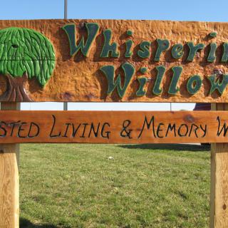 A wooden sign for Whispering Willows Assisted Living & Memory Care.