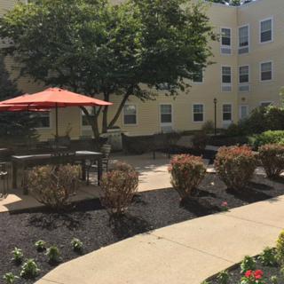 A peaceful patio area with a red umbrella, benches, and lush landscaping outside a residential building.