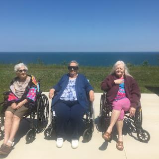 Three elderly women enjoying a sunny day by the sea in their wheelchairs.