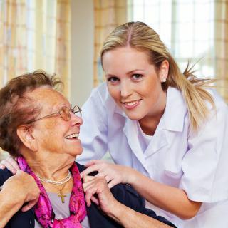A nurse provides care and support to a smiling elderly woman.